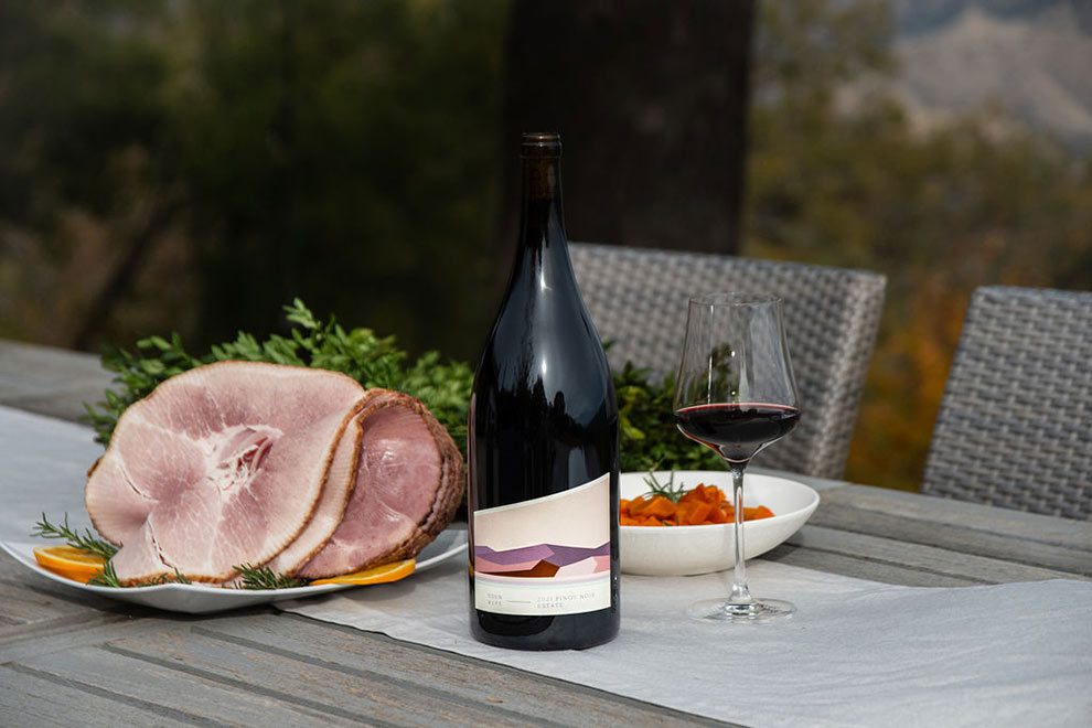 Pinot Noir magnum on a table next to a sliced ham with chairs around the table