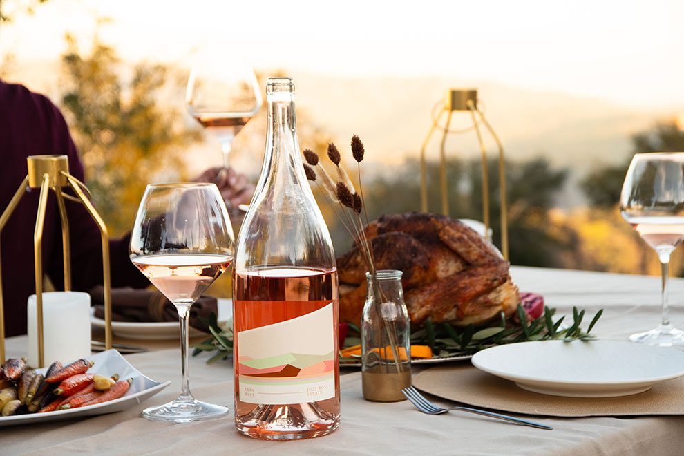 Magnum of Rose on a table with a glass of rose next to it with a chicken and other food and hills in the distance